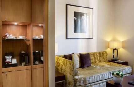 Starhotels Ritz gay-friendly hotel room detail. Cozy seating area with a couch, pillows, lamp, artwork, and a cabinet with a coffee maker.