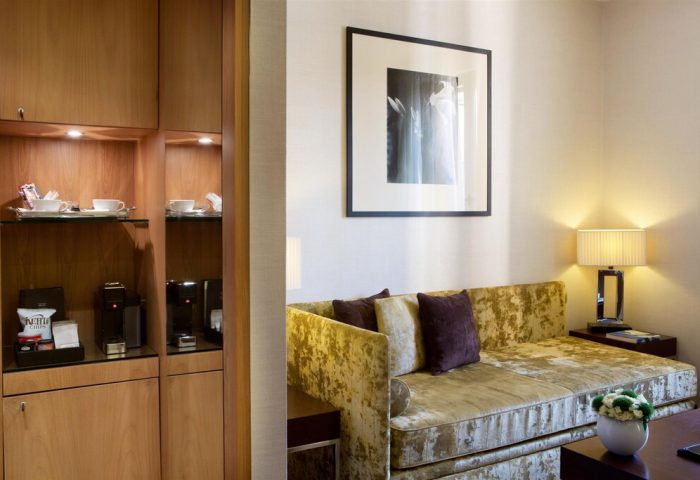 Starhotels Ritz gay-friendly hotel room detail. Cozy seating area with a couch, pillows, lamp, artwork, and a cabinet with a coffee maker.
