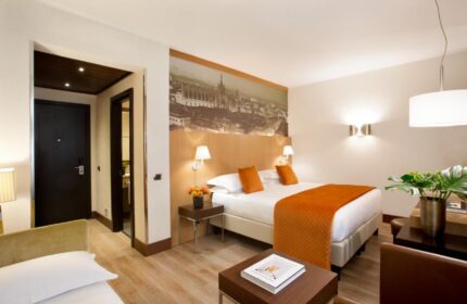 Starhotels Ritz gay-friendly hotel room. Milan hotel bedroom with double bed, orange accents, and city view. Ideal for gay travel in Italy.
