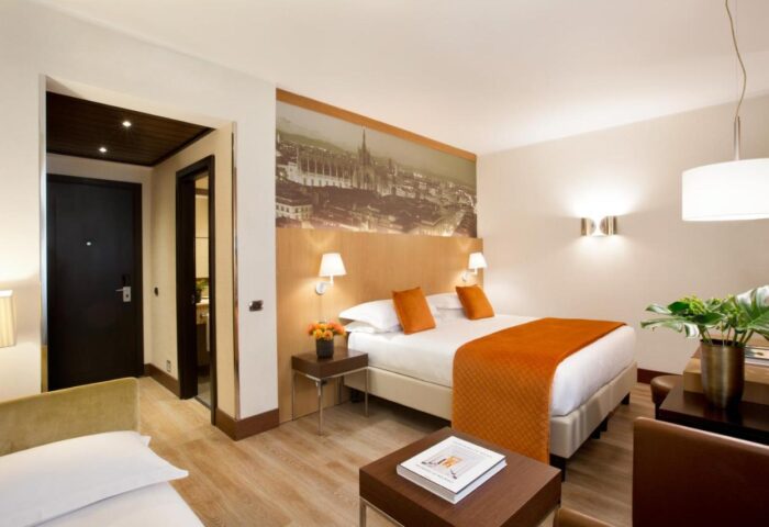Starhotels Ritz gay-friendly hotel room. Milan hotel bedroom with double bed, orange accents, and city view. Ideal for gay travel in Italy.