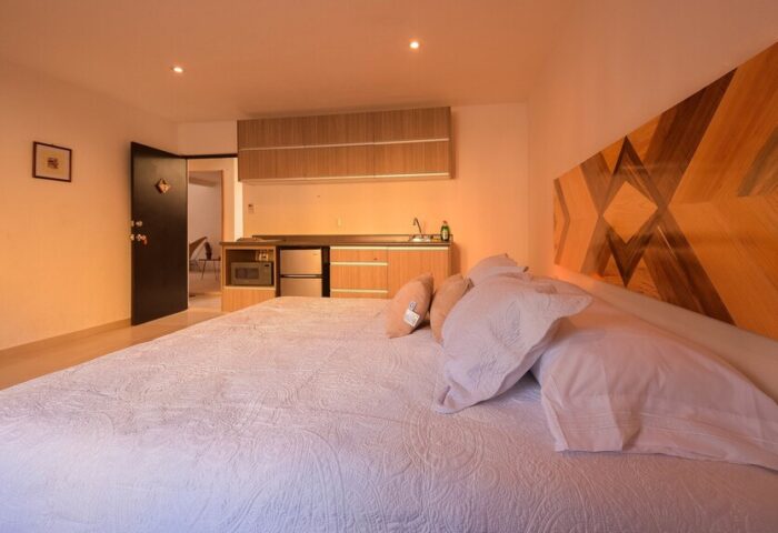 Stay Tropical gay-friendly hotel room: bed with kitchen, microwave, sink, wooden headboard. A cozy space for gay men's travel.