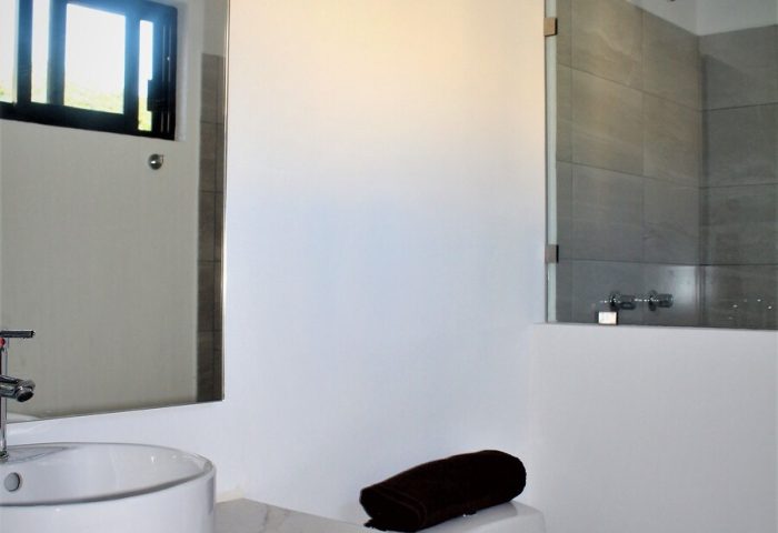 Bathroom at Stay Tropical, a gay-friendly hotel: sink, toilet, and shower with glass door. Modern design for gay men's travel.