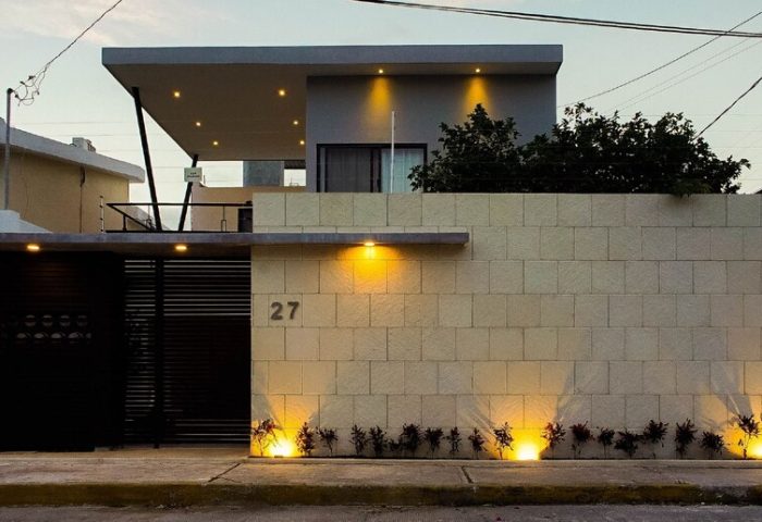 Stay Tropical gay-friendly hotel facade at dusk. Modern architecture, illuminated wall, and gated entrance. Ideal gay travel accommodation.