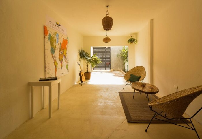 Stay Tropical gay-friendly hotel lobby. World map, guitar, and wicker chairs create a relaxed vibe. Perfect for gay men's travel adventures.