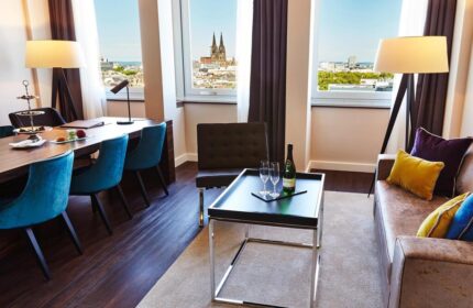 Steigenberger Hotel Köln room. Gay-friendly hotel with city view, table, and sofa. Cologne Cathedral visible. Upscale lodging for gay travelers.