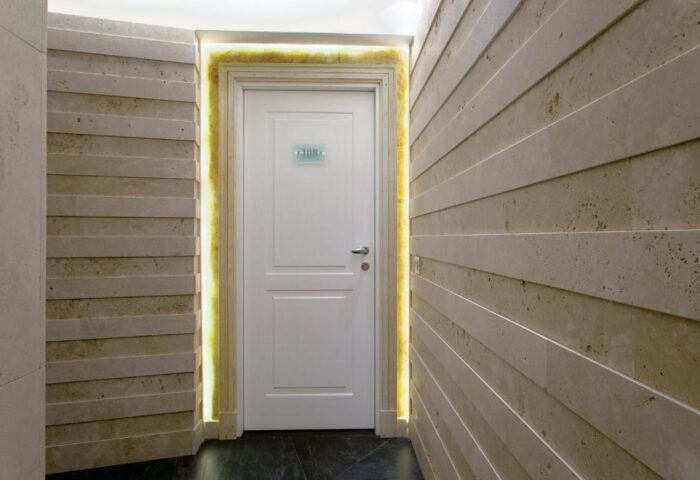 Hallway at Stendhal Luxury Suites, a gay-friendly hotel. White door with room number, stone walls, and soft lighting. Upscale design.
