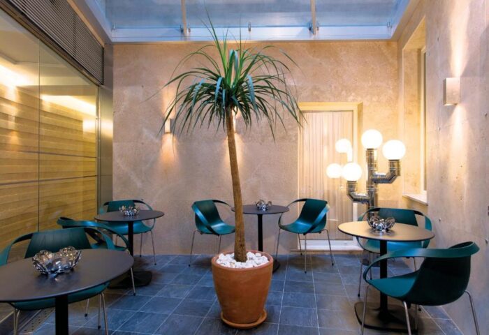 Stendhal Luxury Suites gay-friendly hotel lounge area. Tables and chairs surround a potted tree. Modern design with unique lighting fixtures.