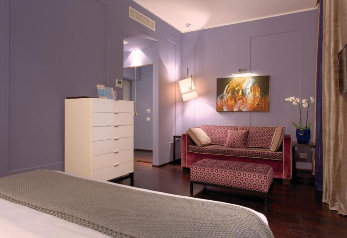 Stendhal Luxury Suites gay-friendly hotel room. Stylish purple walls, patterned sofa & ottoman, modern art, and chic decor for discerning travelers.