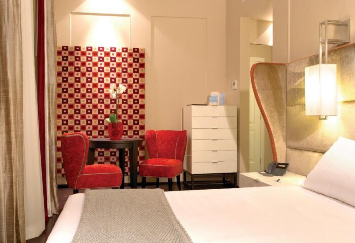 Stendhal Luxury Suites gay-friendly hotel room. Red chairs, modern decor, and a comfortable bed create an inviting atmosphere. Ideal for gay travel.