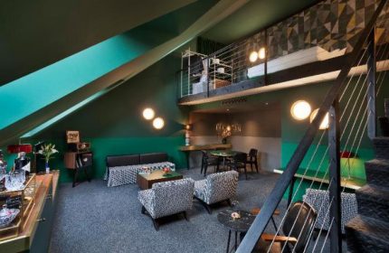 Stories Hotel Budapest gay-friendly room. Loft suite interior with seating area, dining table, stairs, and mezzanine level. Modern design.