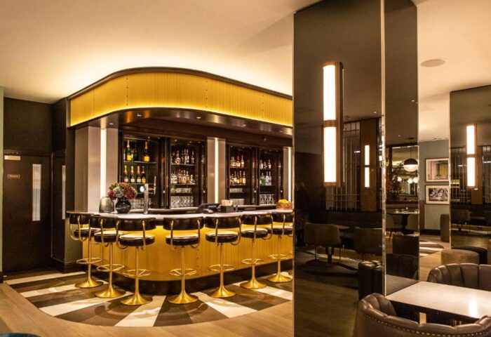 Gay-friendly Strand Palace Hotel bar interior. Gold bar stools, mirrored pillars, and liquor bottles. A stylish hotel for gay travelers.