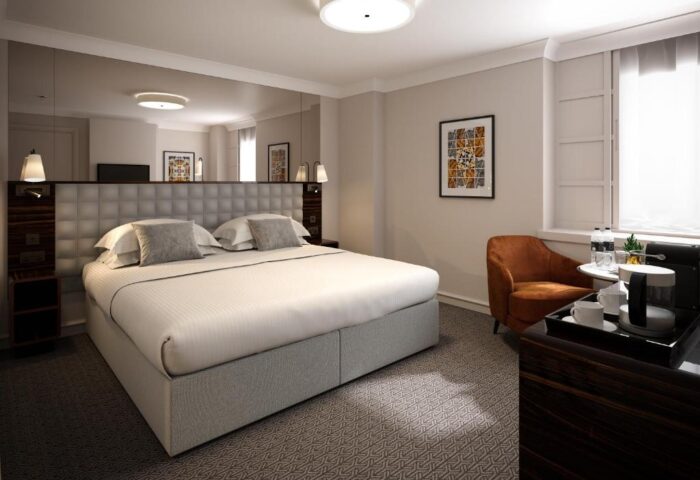 Gay-Friendly Strand Palace Hotel room. Modern interior with a large bed, armchair, and beverage station. Mirror above the bed's headboard.