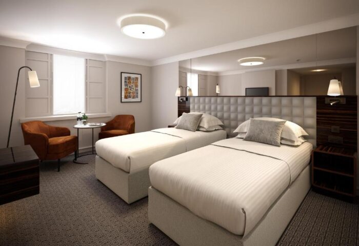 Strand Palace Hotel twin room. Gay-friendly hotel with two beds, chairs, and a table. Ideal for gay travelers seeking comfort in London.
