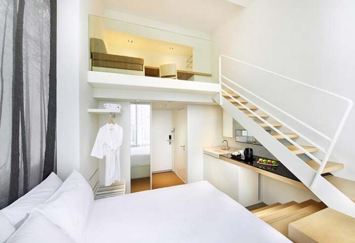 Studio M Hotel's chic loft room. Gay-friendly hotel with modern design, featuring a mezzanine level, kitchenette, and minimalist decor.