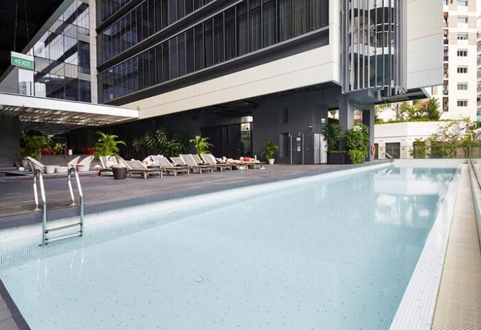 Studio M Hotel's pool, a gay-friendly hotel. People relaxing on deck chairs by the pool. Modern architecture, an urban oasis.