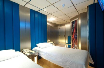 Stylotel, a gay-friendly hotel: Twin beds with white linens, blue padded wall panels, and metallic accents. Modern design for gay travelers.