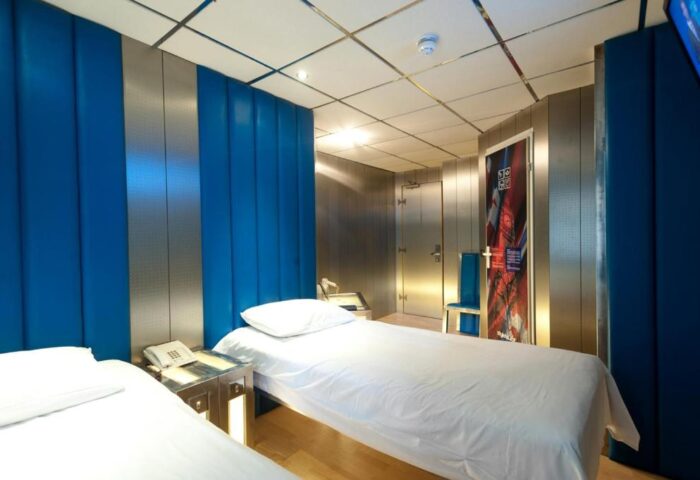 Stylotel, a gay-friendly hotel: Twin beds with white linens, blue padded wall panels, and metallic accents. Modern design for gay travelers.