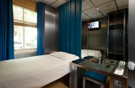 Stylotel, a gay-friendly hotel: Modern room with a single bed, blue accents, and a mirrored wall. A stylish and comfortable space for gay travelers.