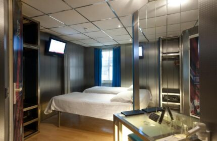 Stylotel, a gay-friendly hotel. Room interior with two beds, TV, wardrobe, safe, and desk. Modern design for gay men travel.