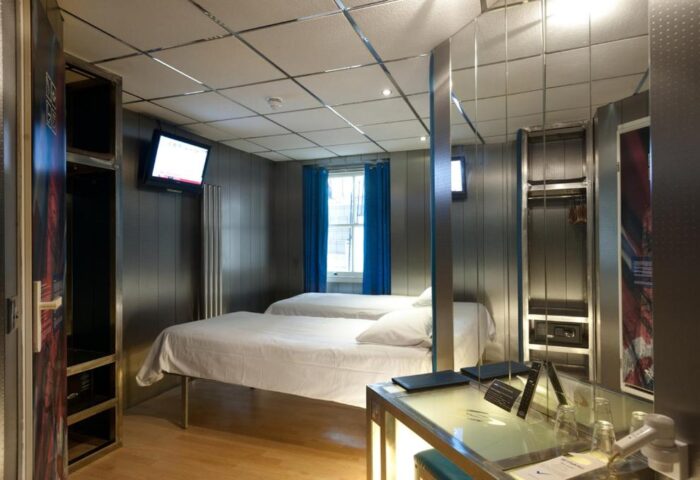 Stylotel, a gay-friendly hotel. Room interior with two beds, TV, wardrobe, safe, and desk. Modern design for gay men travel.