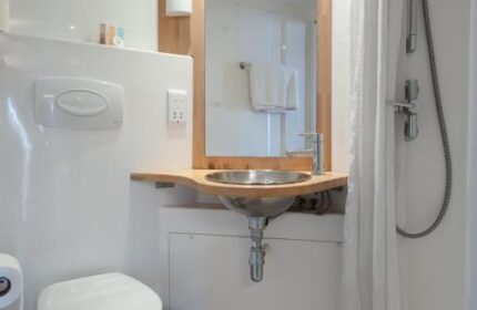 Stylotel bathroom. Gay-friendly hotel room with toilet, sink, mirror, and shower. Modern design with wooden floor and white walls.