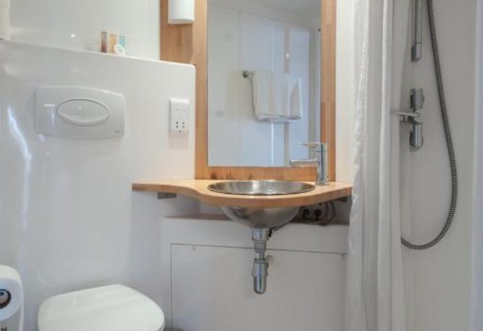 Stylotel bathroom. Gay-friendly hotel room with toilet, sink, mirror, and shower. Modern design with wooden floor and white walls.