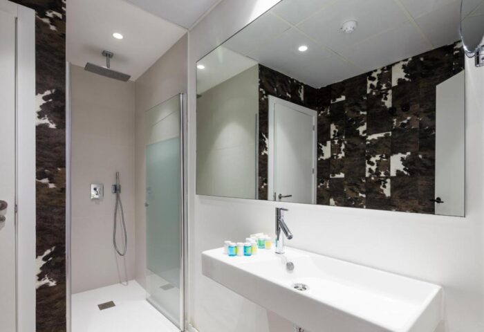 Sud Ibiza Suites gay-friendly hotel bathroom. Modern design with walk-in shower, sleek sink, and stylish cow-print accent wall. Ibiza travel.