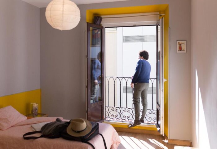 Sungate One, gay-friendly hotel. Man on balcony. Room with bed, backpack, and hat. Travel advice for gay men. Hotel room interior.