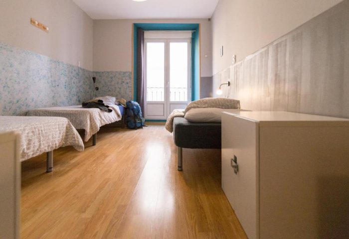 Sungate One gay-friendly hotel room. Twin beds, a backpack, and a balcony are visible. The room has a simple, modern design with wooden floors.