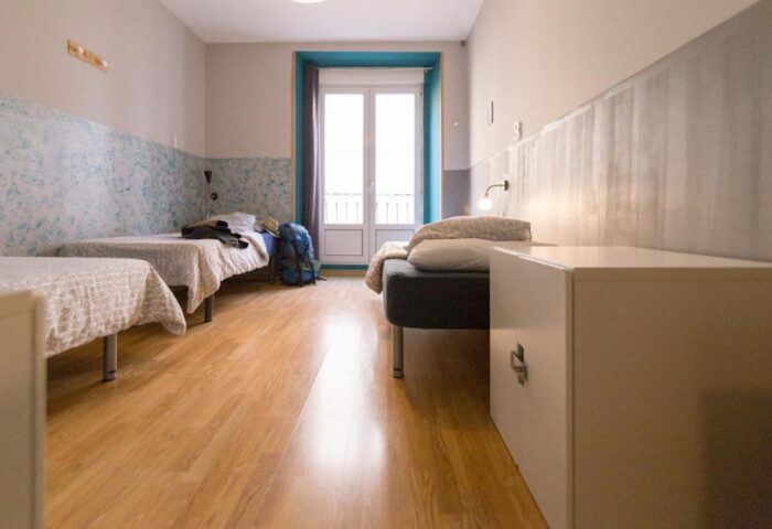 Sungate One gay-friendly hotel room. Twin beds, a backpack, and a balcony are visible. The room has a simple, modern design with wooden floors.