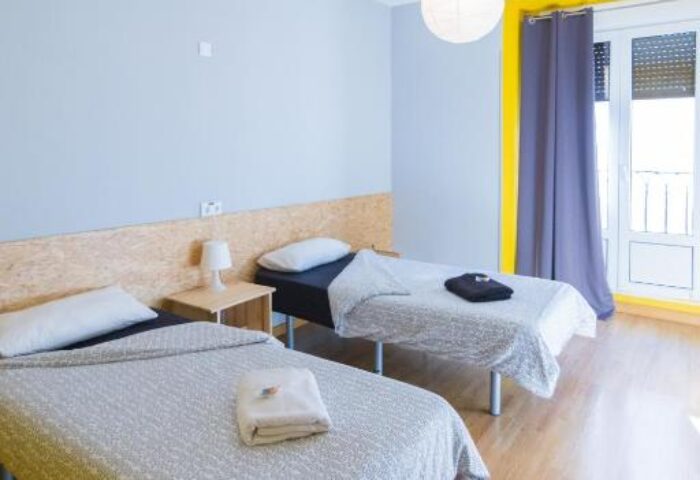 Sungate One gay-friendly hotel room with two single beds, light blue walls, and yellow window frame. Comfortable stay for gay travelers.