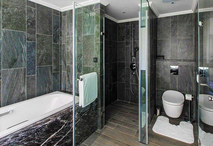 Suz Hotel: Bathroom interior featuring a bathtub, shower, and toilet. Gay-friendly hotel with modern design and dark stone tiles.