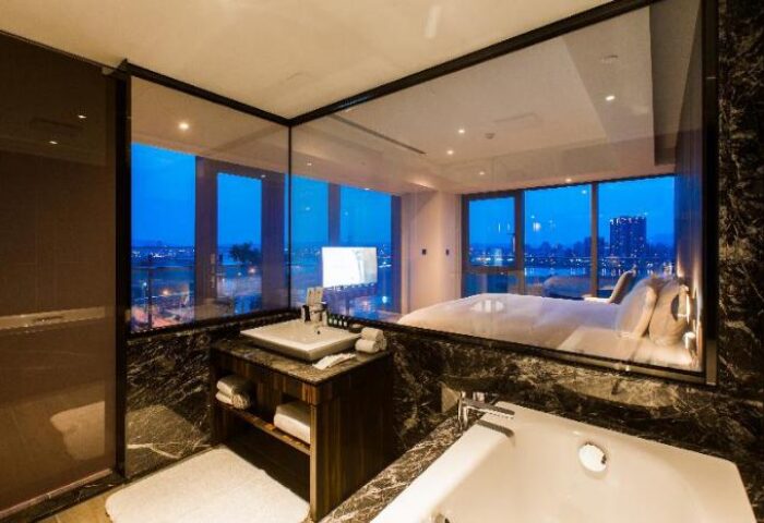 Suz Hotel's gay-friendly bathroom with a view. Modern design featuring a sink, bathtub, and a large window overlooking the city at night.