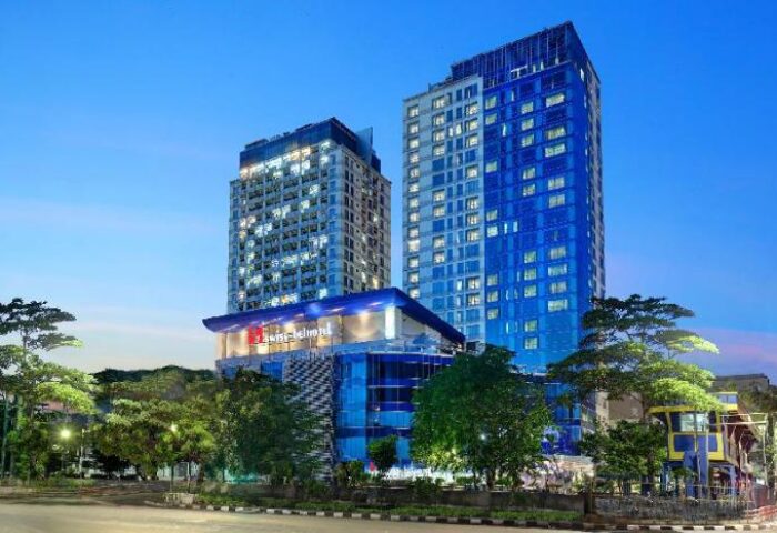 Swiss-Belhotel Mangga Besar exterior view at dusk. Gay-friendly hotel in Jakarta, Indonesia. Modern architecture, blue & white towers.