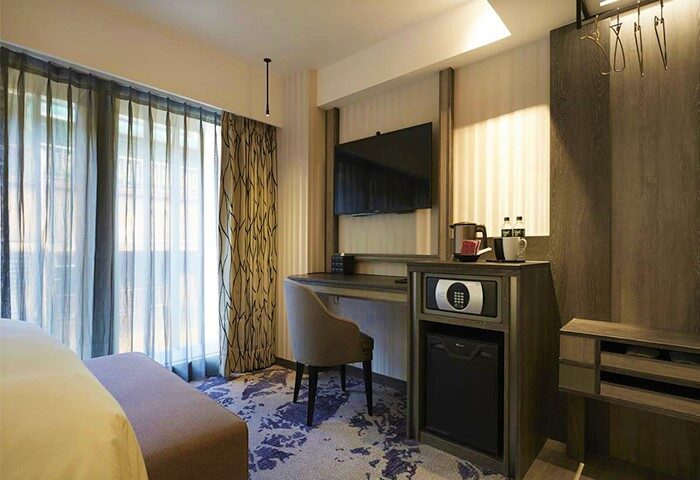 TANGO INN Taipei Ximen room. Gay-friendly hotel room interior with desk, TV, safe, mini-fridge, and patterned carpet. Modern design.