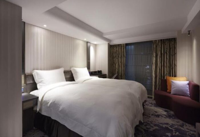 TANGO INN Taipei Ximen gay-friendly hotel room. Double bed with white linens, sofa, curtains, and carpet. Modern design in Taipei, Taiwan.