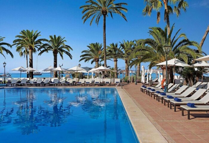 THB Los Molinos Adults Only gay-friendly hotel pool view. Palm trees, lounge chairs, umbrellas, and ocean create a relaxing vibe.