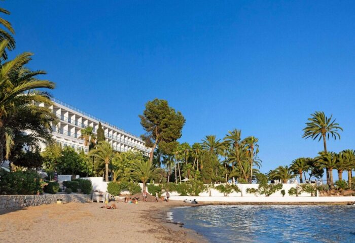 Beachfront view of THB Los Molinos Adults Only, a gay-friendly hotel. Palm trees, sand, blue sky, and ocean create a relaxing vacation scene.