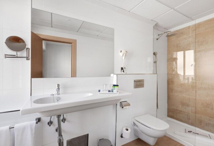 THB Los Molinos Adults Only gay-friendly hotel bathroom. Sink, toilet, shower, mirror, and hairdryer in a modern, well-lit room.