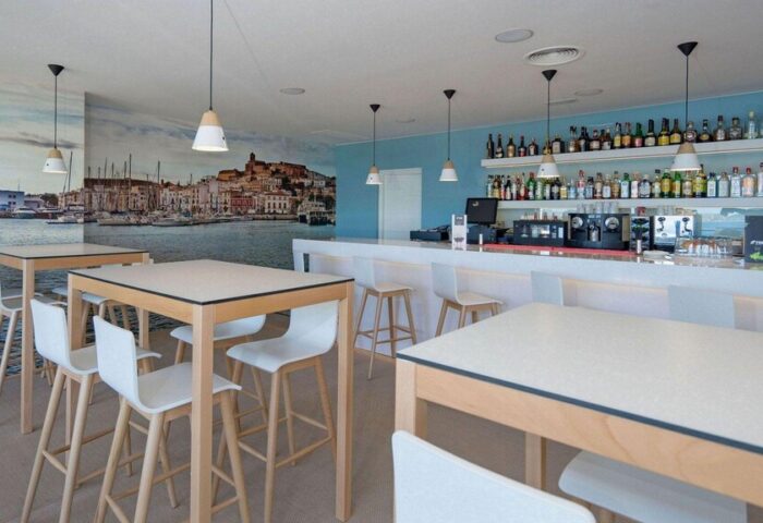 Interior of THB Los Molinos Adults Only gay-friendly hotel bar. Tables, chairs, bar with bottles, and mural of a coastal city.
