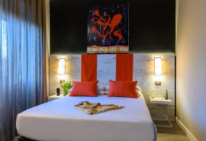 Gay-friendly hotel room: Double bed with orange pillows, abstract art above headboard, bedside tables with lamps. Travel advice for gay men.