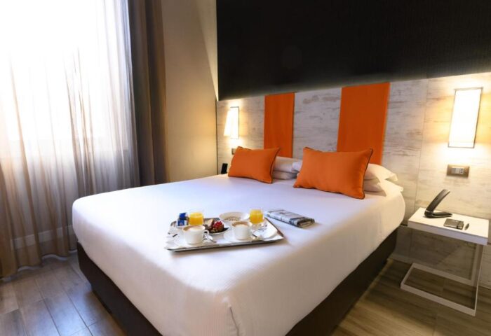 Gay-friendly hotel room, The Guardian. Bed with breakfast tray, orange pillows, and modern decor. Perfect for gay men's travel.