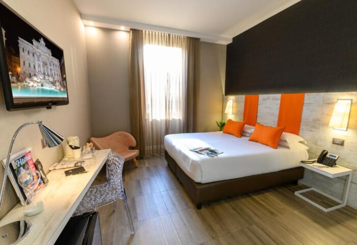 Gay-friendly hotel room. The Guardian travel advice. Modern design with orange accents, desk, tv with fountain image. Gay travel.