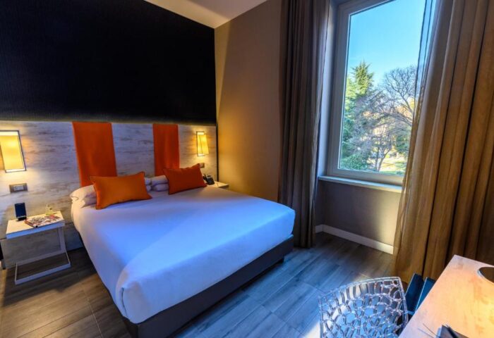 Interior of a gay-friendly hotel room, as featured in The Guardian. Room view with king bed, orange accents, and window overlooking trees.