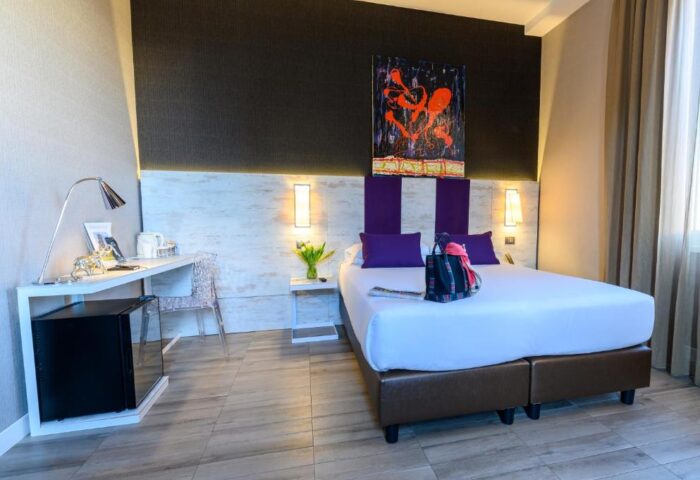 Gay-Friendly Hotel bedroom. Modern decor, desk, bed with purple accents, abstract art. Gay travel lodging, The Guardian recommended.