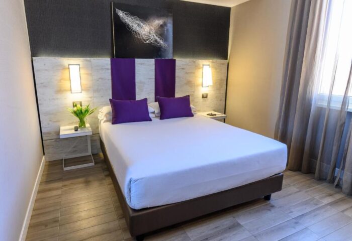 Gay-friendly hotel room, The Guardian. Modern design with a double bed, purple accents, bedside tables, and abstract art. Comfortable for gay travelers.