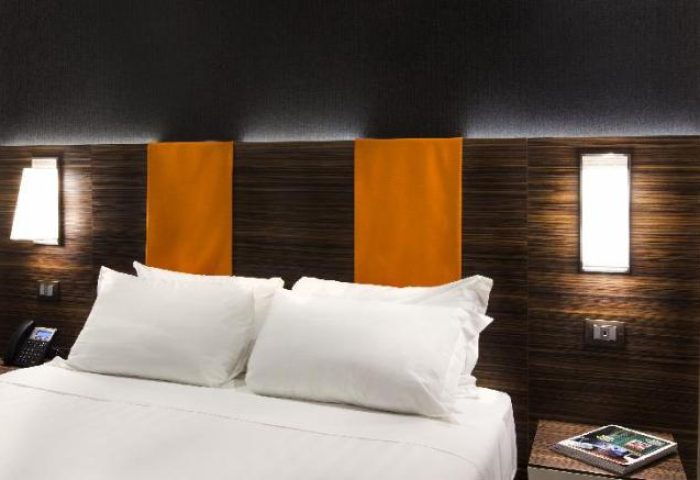 Bedroom at The Republic, a gay-friendly hotel. Modern design with white linens, dark wood headboard, and orange accents. Nightstand with book.