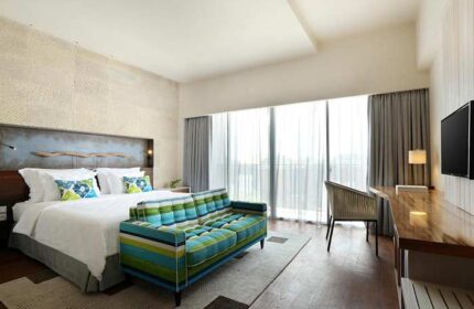 TS Suites Seminyak gay-friendly hotel room. Modern design featuring a bed, striped couch, desk, and large windows. Upscale accommodations.
