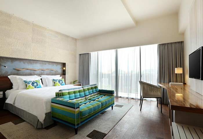 TS Suites Seminyak gay-friendly hotel room. Modern design featuring a bed, striped couch, desk, and large windows. Upscale accommodations.