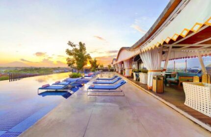 TS Suites Seminyak gay-friendly hotel rooftop infinity pool at sunset. Lounge chairs line the pool's edge, with a covered bar area nearby.
